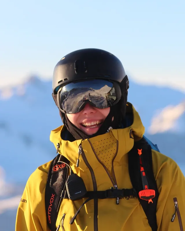 Niklas Meindl in a yellow shell, helmet and goggles, on a snow ridge at last light